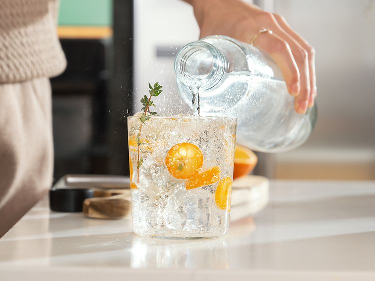 person heller boblefann fra en flaske over i et glass med frukt og isbiter
