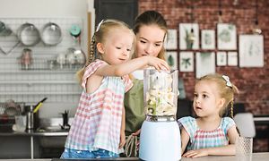 Two kids making smoothies with their mother