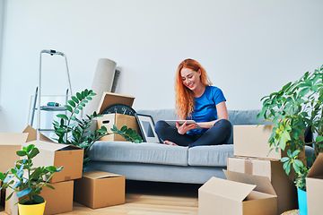 en ung kvinne sitter i en sofa med flytteesker rundt seg