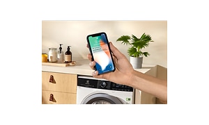 Hand holding a smartphone in front of a Electrolux washing machine