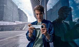 En fyr spiller på en hvit ROG Phone 6 ute i regnet ved siden av et glassvindu