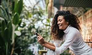 Smilende kvinne på balkong som ser på smarttelefon