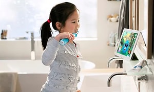 Jente som børste tennene med elektrisk tannbørste mens hun ser på et nettbrett