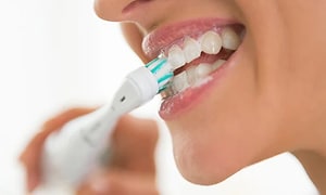 Nærbilde av person som børster tennene med elektrisk tannbørste