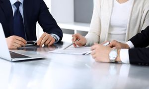 Forretningsfolk diskuterer kontrakt på møte sittende rundt et skrivebord