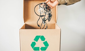 En pappboks med resirkuleringssymbol og en hånd som plukker opp en ledningsknute fra den