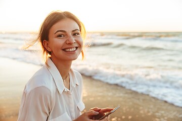 Smiling woman on beach holding smartphone