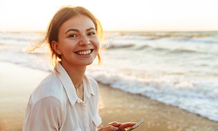 Smiling woman on beach holding smartphone
