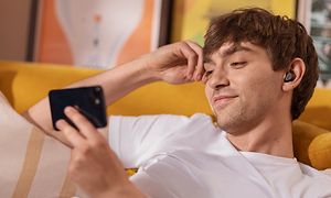 Mann med Jabra Elite 5 i ørene på en sofa som holder en smarttelefon