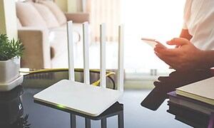 hvit router i stue med person som holder smarttelefon