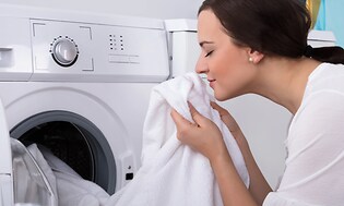 Kvinne som lukter på klesvask fersk fra tørketrommelen