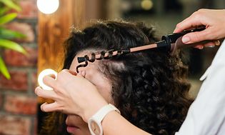 Hair stylist curling woman's black hair with a curling iron in beauty salon