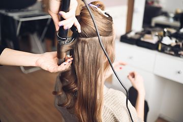 Hair stylist making curls in the hair of a woman with a curling iron in beauty salon