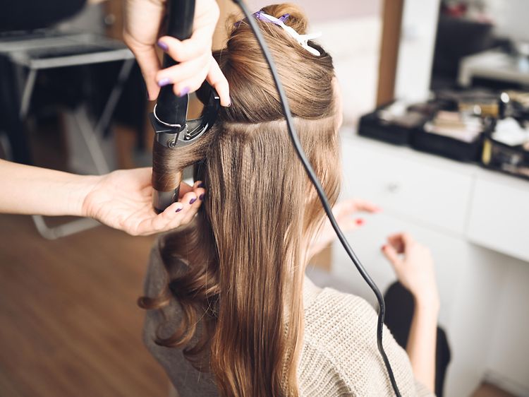 Hair stylist making curls in the hair of a woman with a curling iron in beauty salon