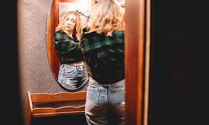 Young woman using curling iron looking at herself in the mirror