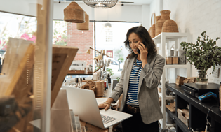 B2B - Elkjøp Control - A woman speaking on her smartphone in front of her laptop in a shop