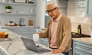 En mann på et kjøkken holder en kaffekopp over sin HP 14 Chromebook