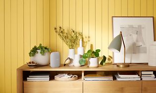 Google Nest Audion standing on a sideboard with lots of plants and decorations beside it