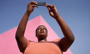 Woman holding Pixel 6a with pink building and sky behind