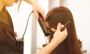 Woman with long brown hair in beauty salon with hair dresser using hair straightener
