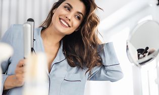 Woman with brown curly hair holding straightening iron