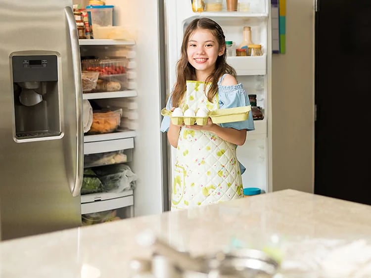Jente henter egg fra et kjøleskap med to dører