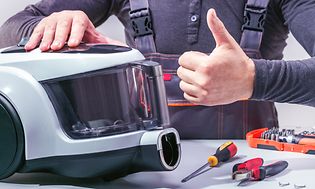 Man repairing a vacuum cleaner with a thumbs up