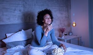 Woman eating popcorn while watching TV in bed