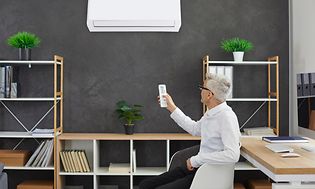 SDA - Heat pump - Businessman is sitting on a chair in his office controlling heat pump with a remote