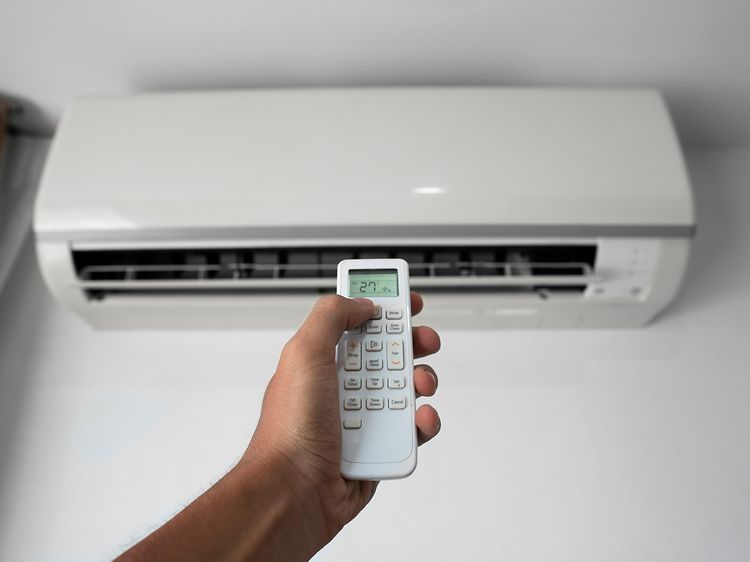 Man's hand holding remote controller pointed towards heat pump