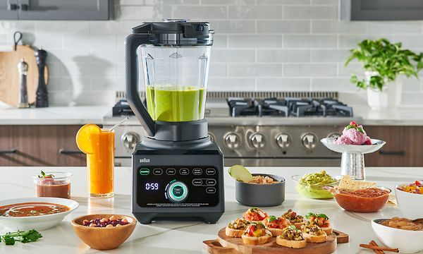 En Braun TriForce Power blender med grønn smoothie og mat på et bord på et kjøkken