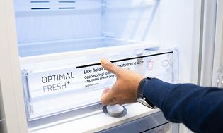 Man's hand opening the drawer at the bottom of an open fridge