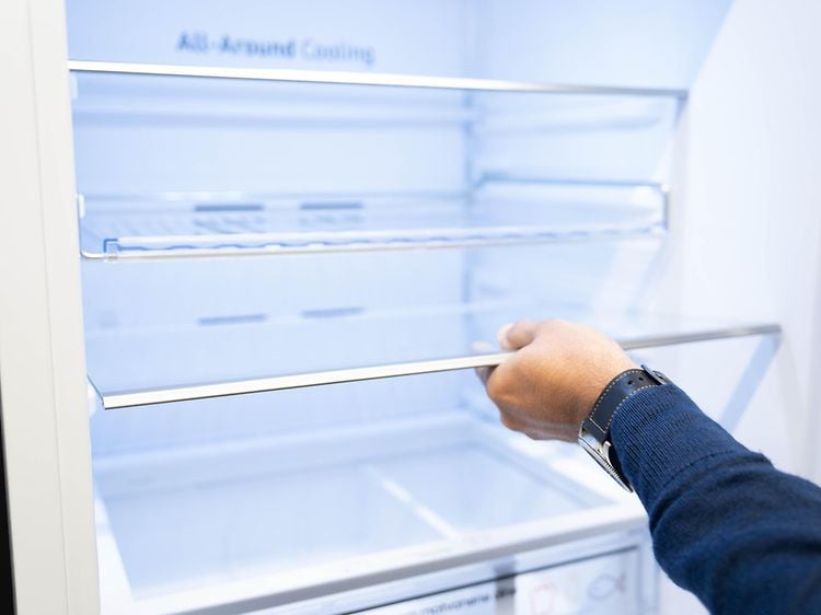 Man's hand holding the shelf of a fridge