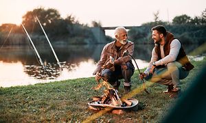 Men grilling fish by river