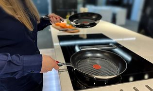 Woman holding two frying pans over a stove