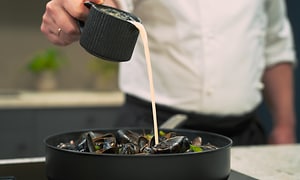A chef pours sauce into a high rimmed pan