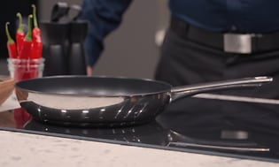 A frying pan on a hob with a man in the background