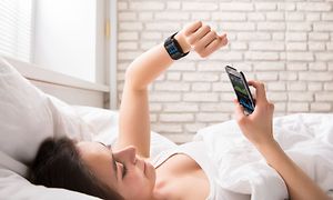 Telecom - Workout - woman in bed looking at her heart rate monitor and her phone