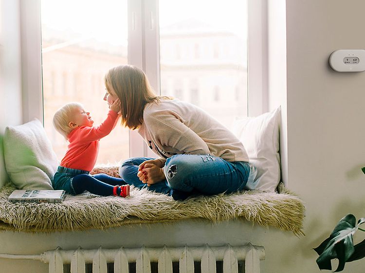 En mor og et barn som koser seg sammen og en Airthings luftkvalitetsmonitor på veggen