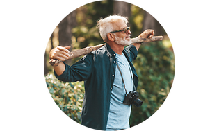 An old man with a camera holds a stick on his shoulders in a forest