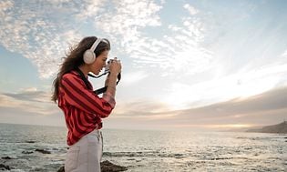 Ung kvinne på stranden med hvite Bose-hodetelefoner og tar bilder