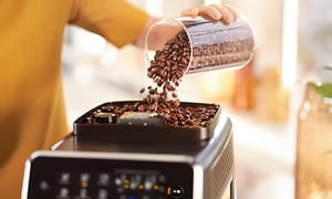 Person som heller kaffebønner over på en Philips Espressomaskin