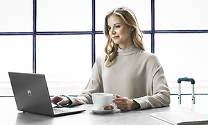 kvinne sitter foran bord med kaffekopp og laptop