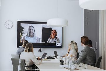 Office - B2B - people attending a hybrid meeting with laptops and a large screen