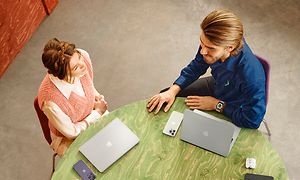 Mannlig Elkjop-ansatt snakker med en kvinne ved et bord med Apple-produkter