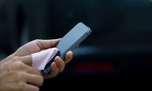 Person holder smarttelefon og rengjør skjermen med en pusseklut