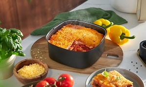 Philips Airfryers separate bakeform med nystekt lasagne på et bord ved siden av ferske grønnsaker og basilikum