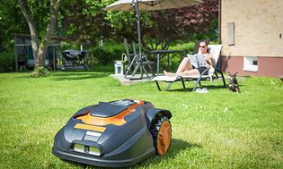 Woman relaxing in the garden and a robot lawn mover cutting the lawn