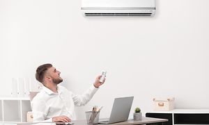 Man adjusting heat pump with a remote control in the office