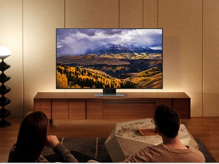 Et par som sitter i en sofa og nyter Samsung TVs sterke farger for rikere visning